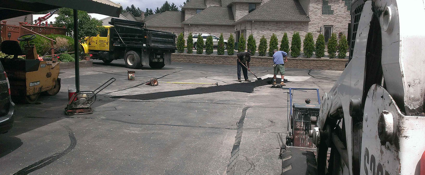 Central Seal Coat employees working on a Parking lot asphalt repair with a asphalt spreader